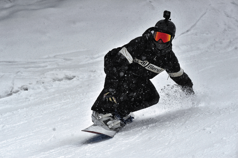 snowboarder wearing all black and a go-pro while going down the mountain