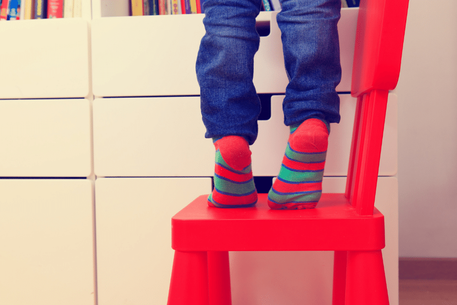 Child on a chair trying to climb to reach the top bookshelf