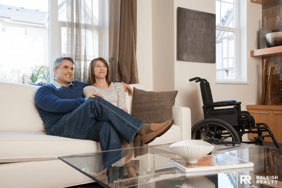 Disabled husband and wife watching tv on the couch with wheelchair next to them