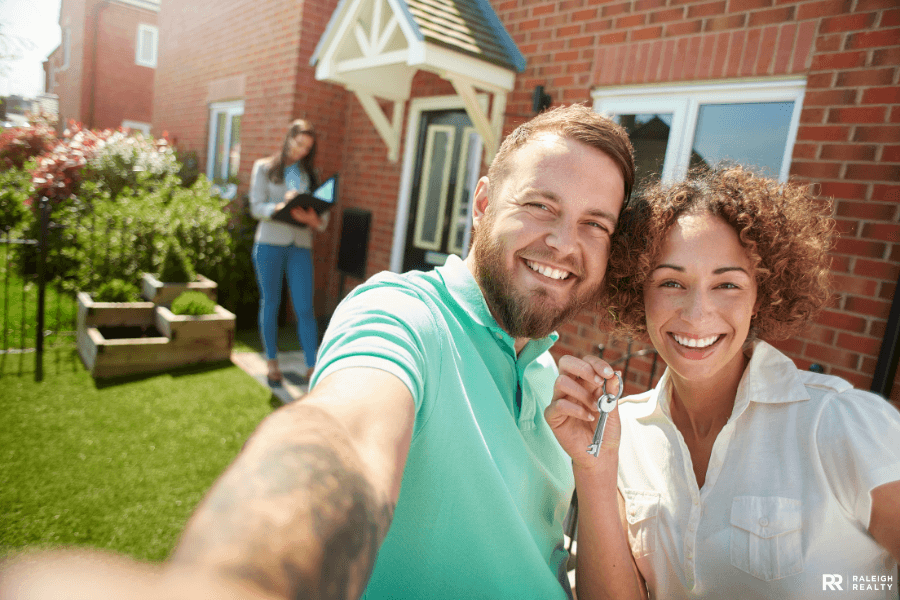 Two happy first time home buyers who have purchased their first house immediately after graduating from college and holding the keys with real estate agent in the background