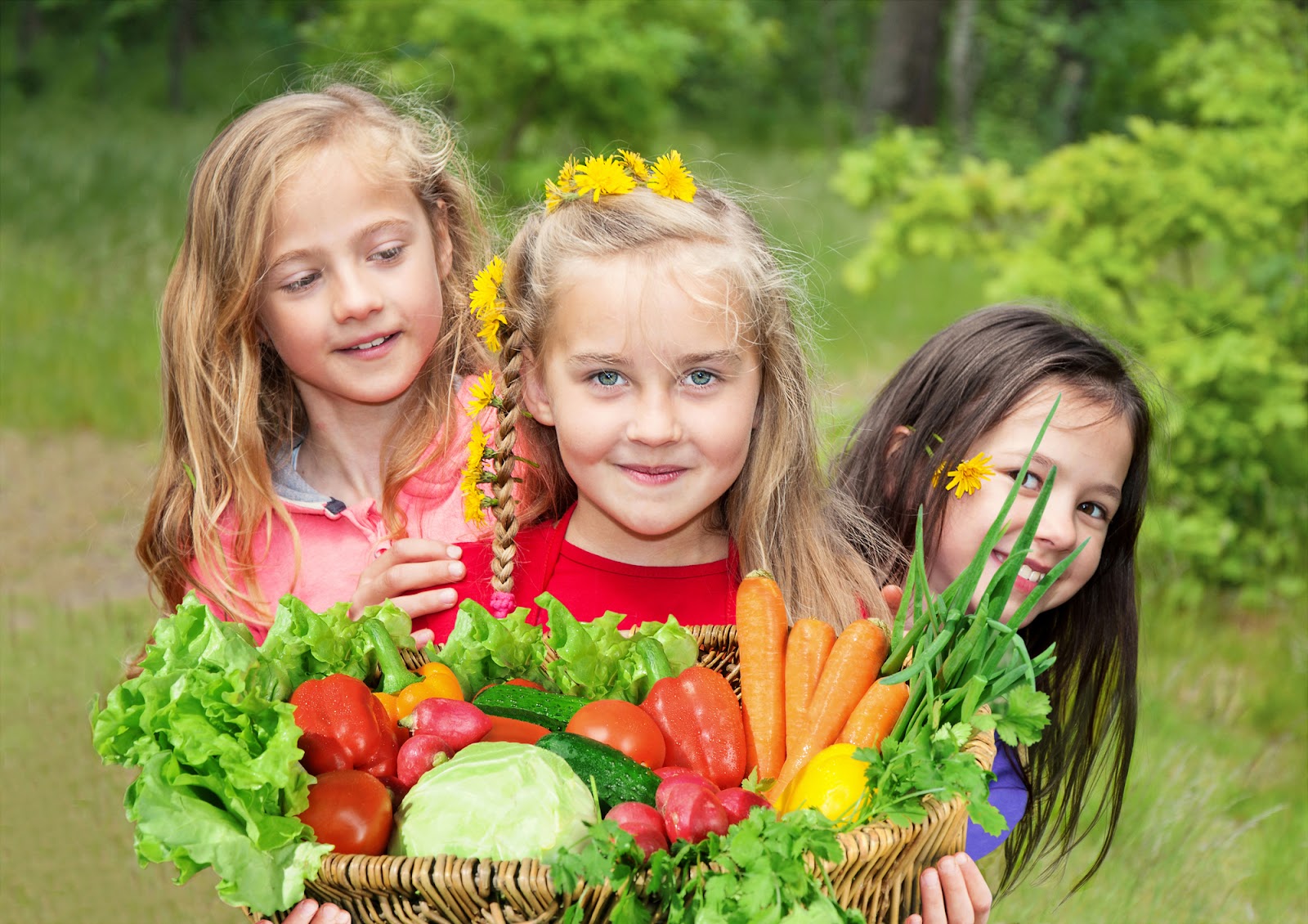 Three children smile as they hold a basket of vegetables.