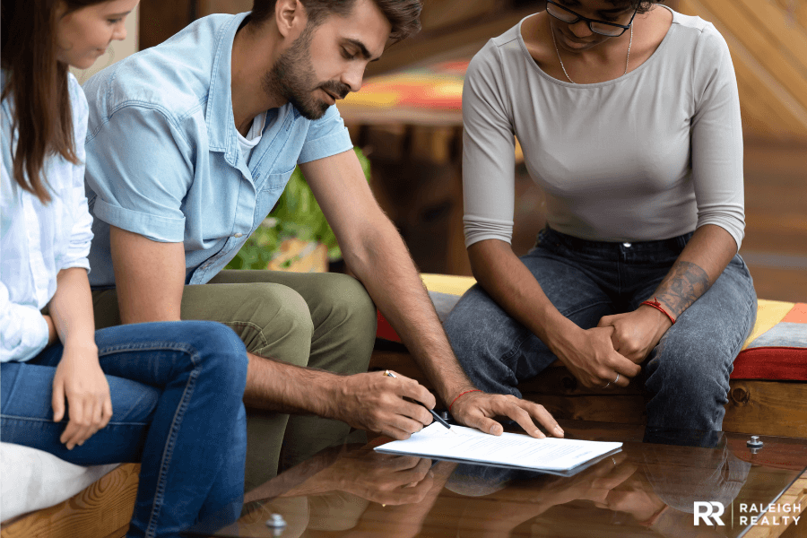 Home buyers signing a real estate contract with a real estate agent looking on