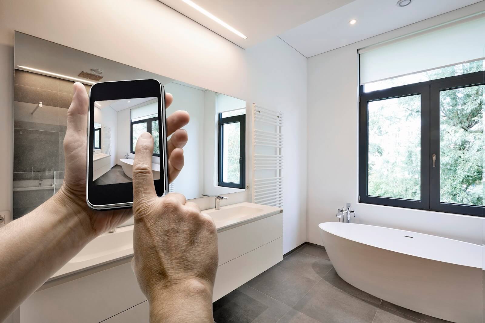 A closeup of a person’s hands taking a picture of their updated bathroom.