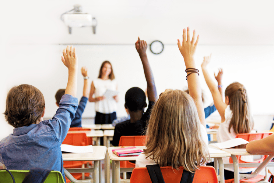 students in class raising their hands to answer a question