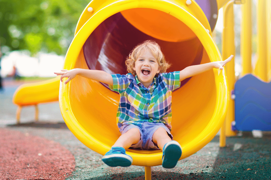 Young kid playing on a playground and going down a yellow slide