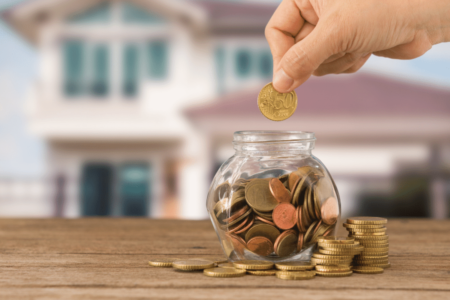 Photo of a money jar with a home in the background explaining The hidden costs when buying a house 