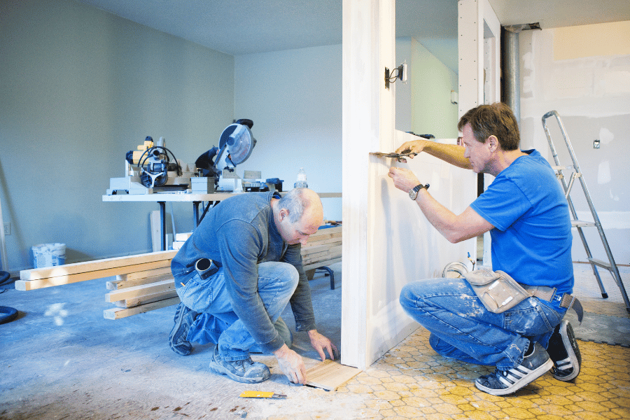 Two people renovating a home by working on the floors and the walls