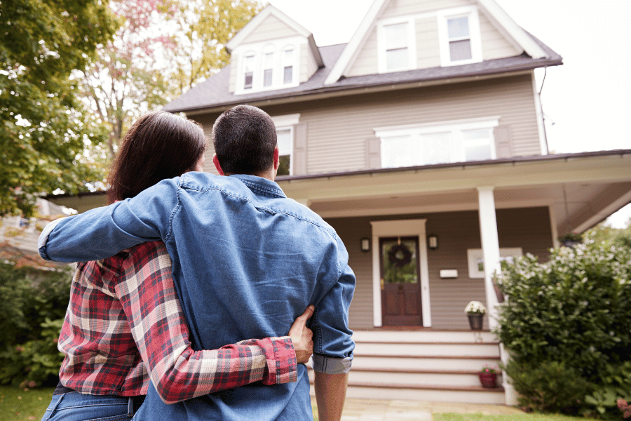 couple buying first home and standing in front of it 