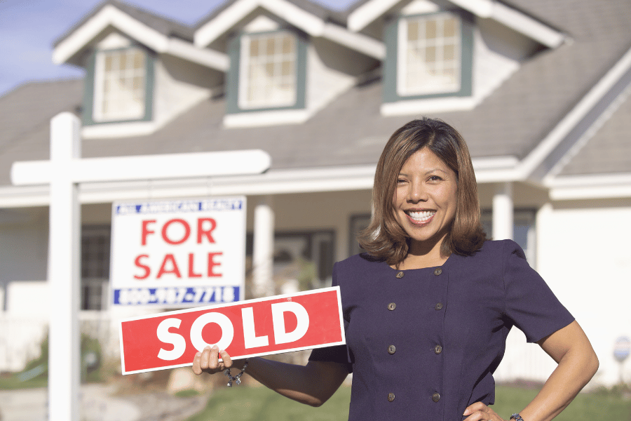Real Estate Agent Holding Sold Sign In Front of House 