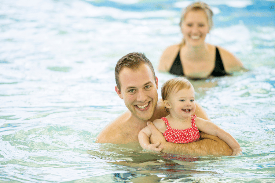 family swimming in pool with young child