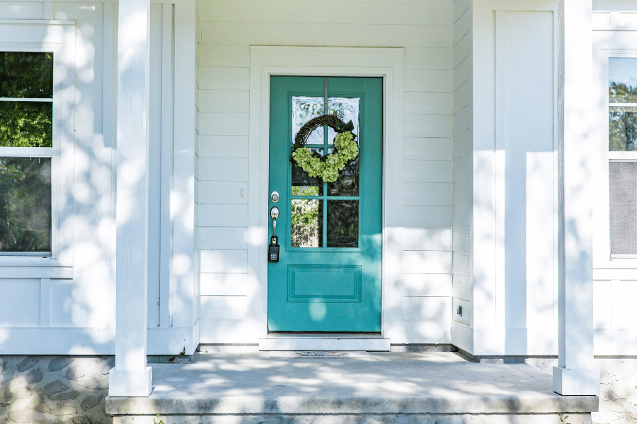 pretty turquoise front door with windows on a white house with a lockbox