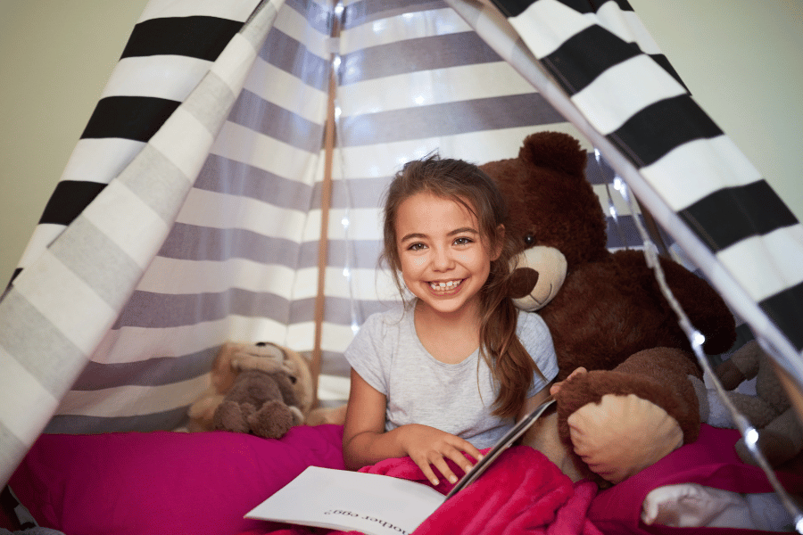 young girl reading a book in her book nook with stuffed animals
