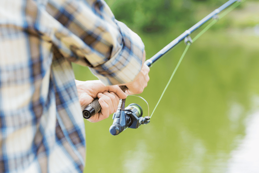 Close up of someone fishing with a fishing pole wearing a flannel