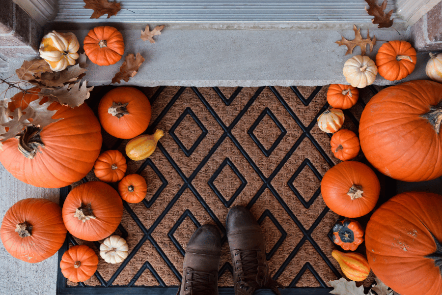 decorative welcome mat on front porch surrounded by pumpkins