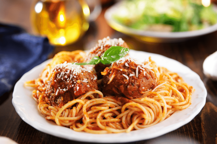 Spaghetti and Meatballs in a white bowl with salad in the background