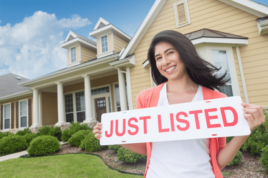 woman holding a 'just listed' sign infront of a home