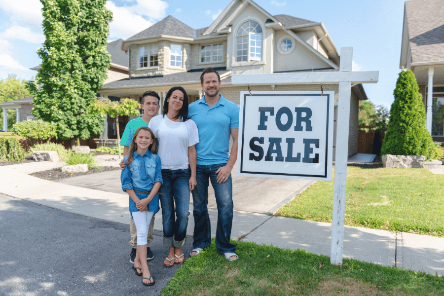 family of four standing in front of house and for sale sign