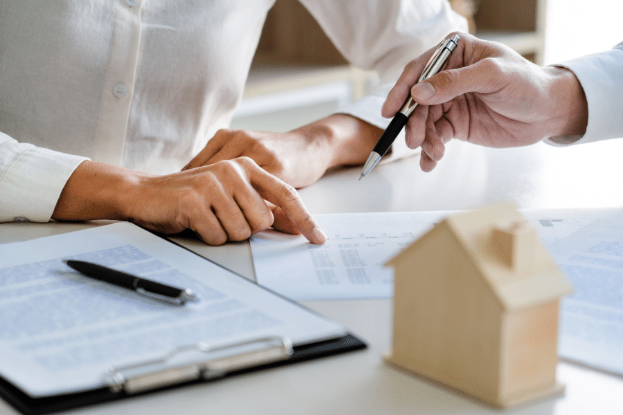 Paper, pens, and a wood toy house on a white desk 