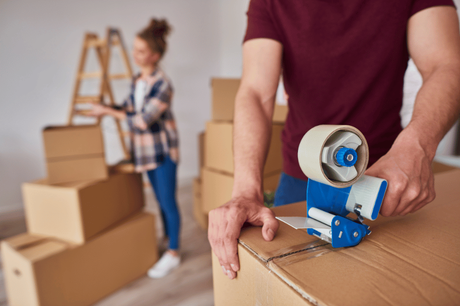 Couple packing boxes and taping them shut during their move 