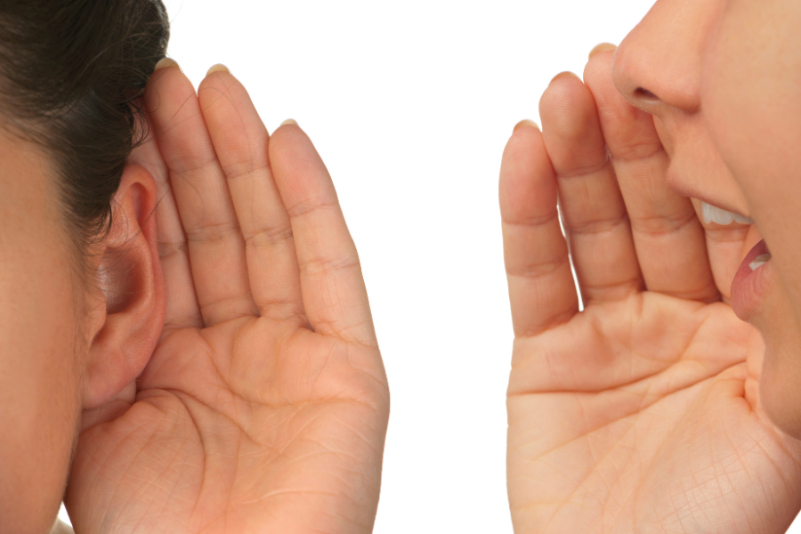Photo of hand cupped around ear and another person speaking into ear of another